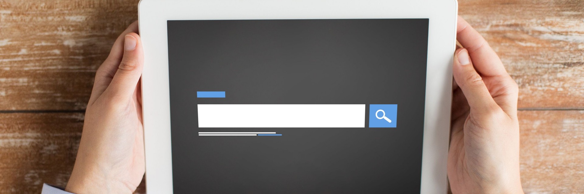 A man holding a tablet with a search bar on it while resting on a desk of reclaimed wood