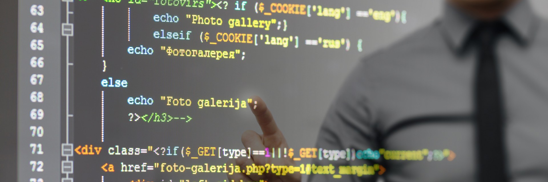 Code on a transparent touch screen with a programmer dressed in a tie in the background